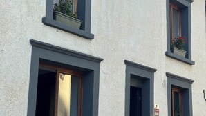 A building with three windows, each with a flower box. There is a door with a sign indicating an alarm system.