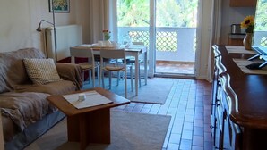 A living room with a sofa, coffee table, and a dining area with chairs and a table. There is a kitchen area with cabinets and a countertop. - Helle Wohnung mit Balkon im Grünen in Strandnähe (La Croix-Valmer)