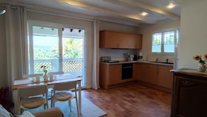 A compact kitchen with wooden cabinets, a dining table with chairs, and a view of greenery through the windows. - Helle Wohnung mit Balkon im Grünen in Strandnähe (La Croix-Valmer)