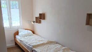 A bedroom with two single beds, a wooden nightstand, a small table, and a window with blinds. - Helle Wohnung mit Balkon im Grünen in Strandnähe (La Croix-Valmer)