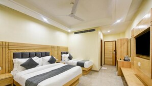 Une chambre d’hôtel avec deux lits, des têtes de lit en bois, un ventilateur de plafond, une télévision et un banc.