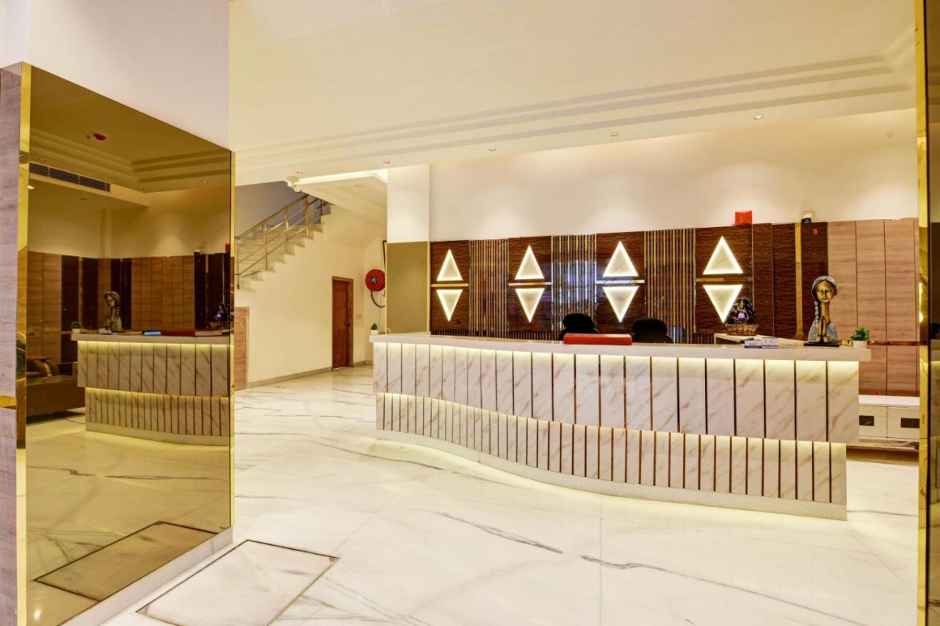 A hotel reception area with a marble floor, a reception desk with a modern design, and a staircase in the background.