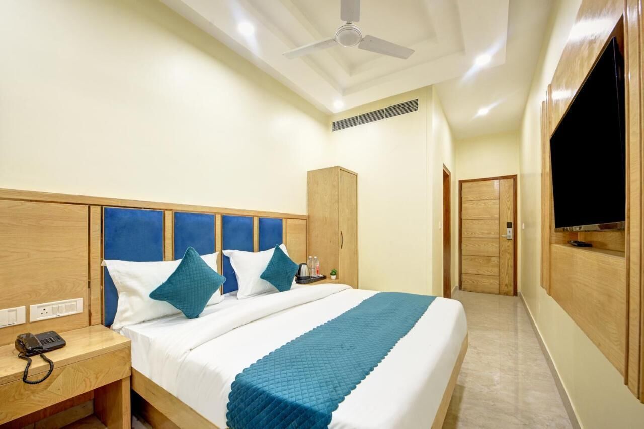 A hotel room with a bed, wooden headboard, a nightstand with a phone, a TV mounted on the wall, and a wardrobe.