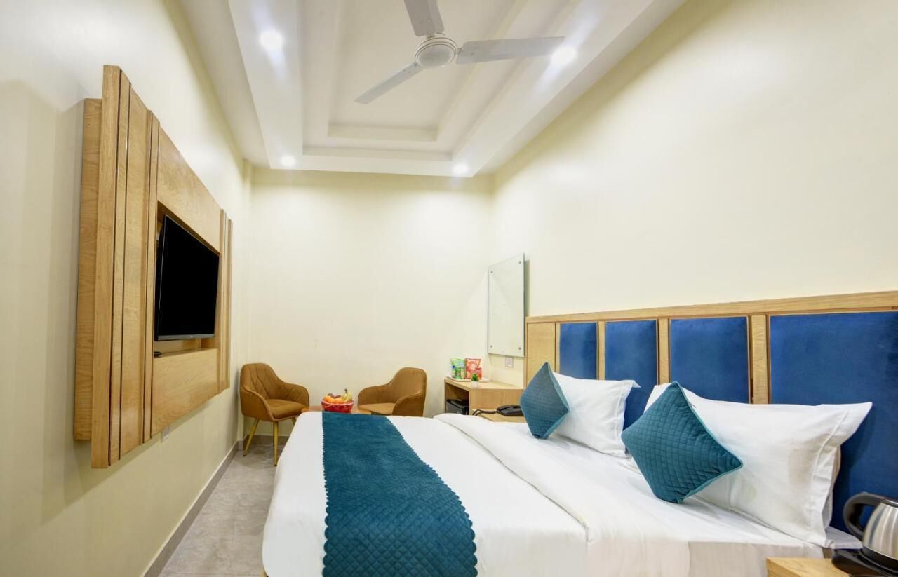 A hotel room with a bed, a TV mounted on the wall, a ceiling fan, and a desk with a chair.