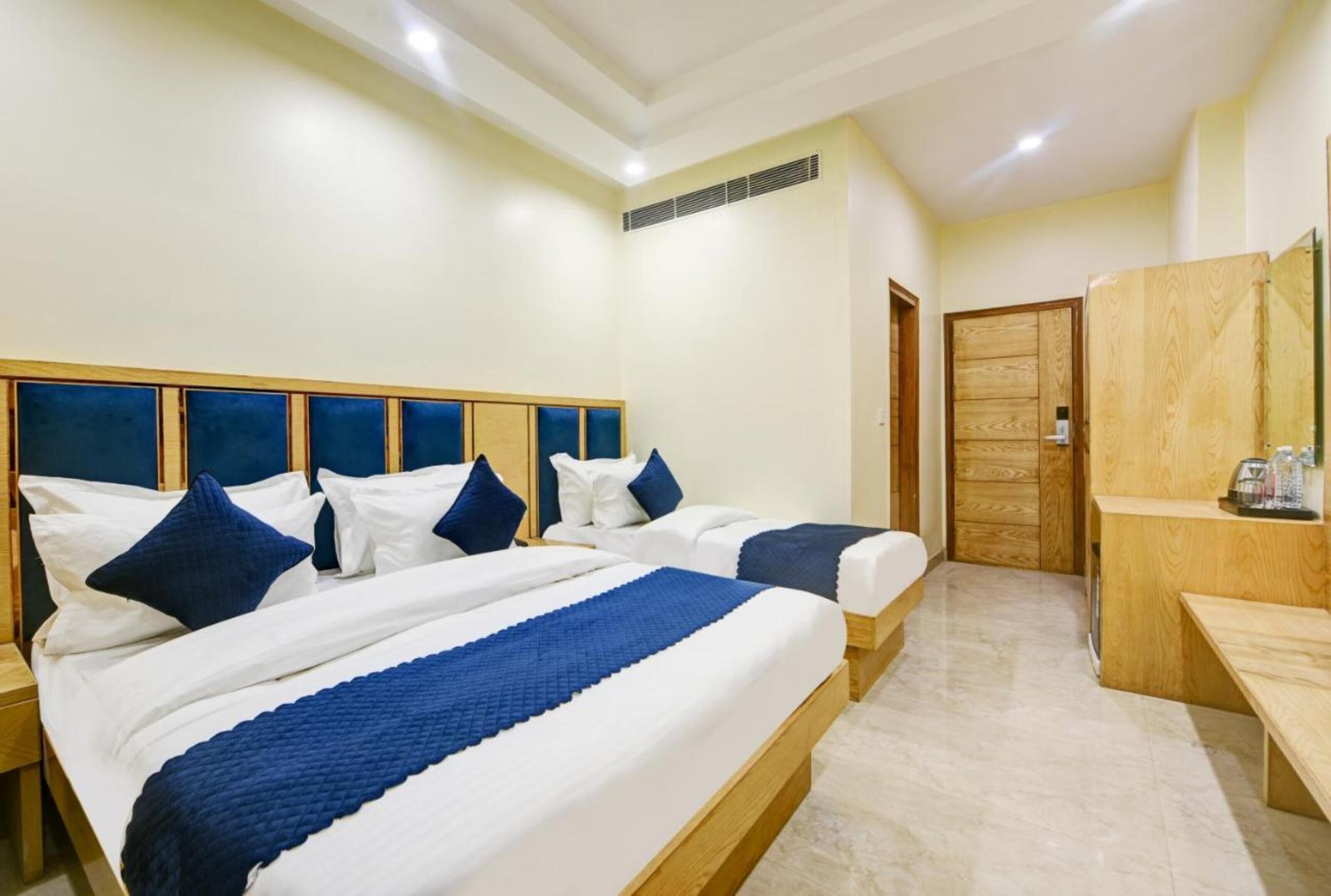 A hotel room with two beds, a wooden headboard, a wooden bench, and a small table with a kettle.