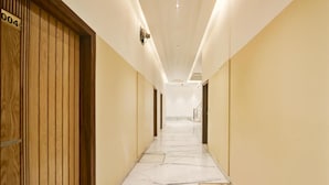 Un couloir d’hôtel avec des portes en bois, un sol en marbre et des luminaires encastrés.