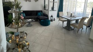 Een moderne woonkamer met een hoekbank, een eettafel met stoelen en een decoratieve plantenopstelling.