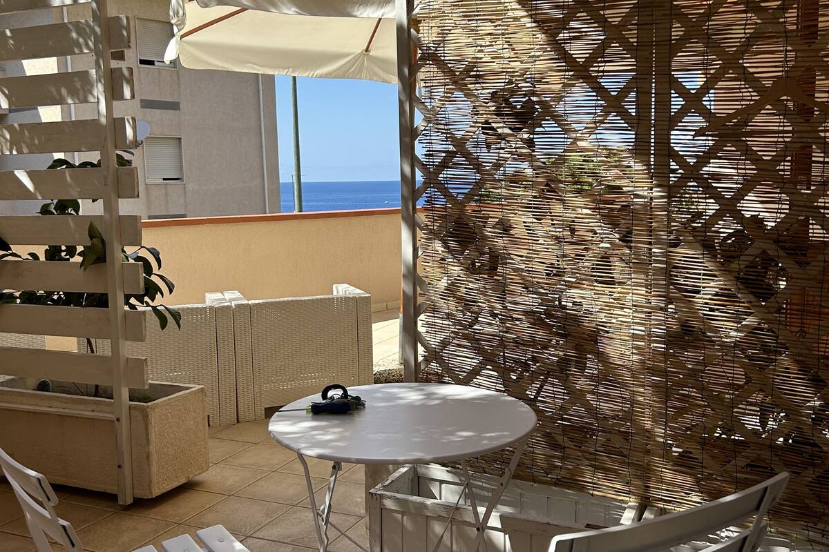 Un patio exterior con sillas y mesa de metal blanco, una sombrilla blanca y un separador decorativo de bambú.