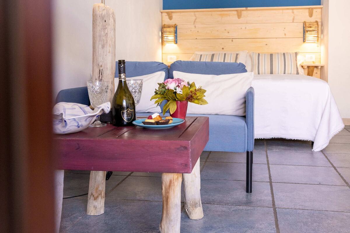 Un dormitorio con una pared azul de acento, un cabecero de madera, una mesita de noche con una lámpara, una botella y un arreglo floral.