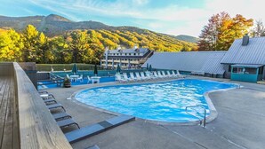 Una piscina con sillones de descanso, una terraza de madera y vistas a una montaña y árboles.