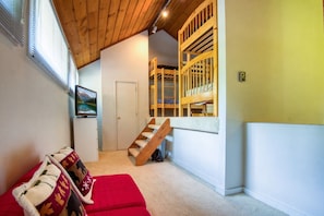 A room with a red sofa, a wooden staircase, and a TV on the wall.