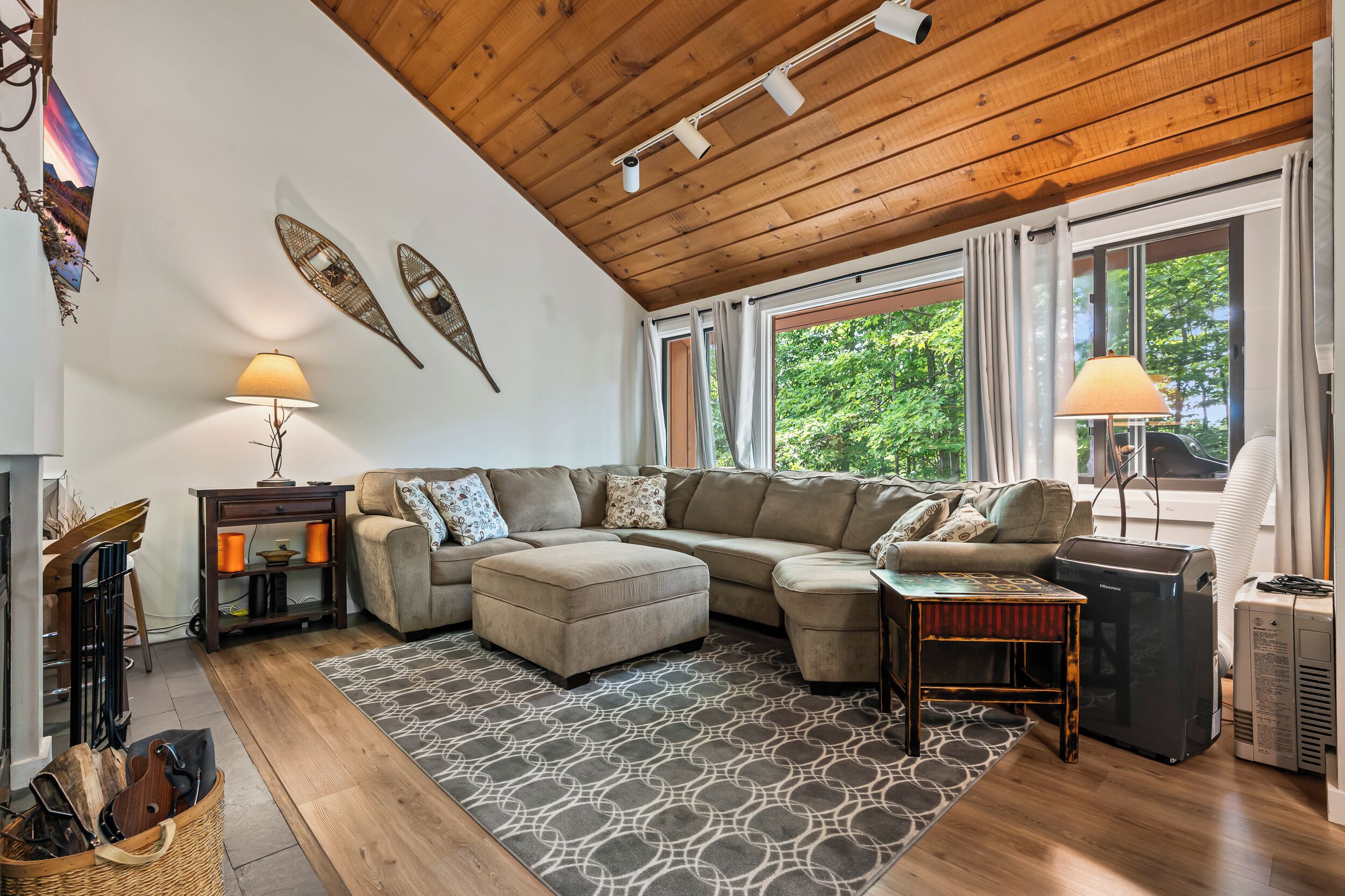 A cozy living room with a sectional sofa, a patterned rug, and a wooden ceiling.
