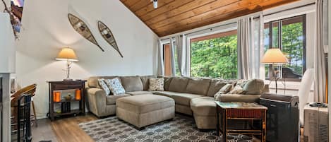 A cozy living room with a sectional sofa, a patterned rug, and a wooden ceiling.