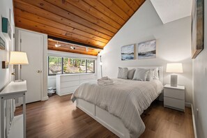 A bedroom with a wooden ceiling, a bed with a white headboard, two bedside lamps, and a window with a view of greenery. - The Village Lodge - Loon Mountain - Pools - Skiing - Mountain Biking - Shopping (Lincoln)