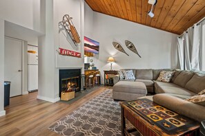 A modern living room with a fireplace, a sofa set, decorative wall art, and a wooden ceiling. - The Village Lodge - Loon Mountain - Pools - Skiing - Mountain Biking - Shopping (Lincoln)