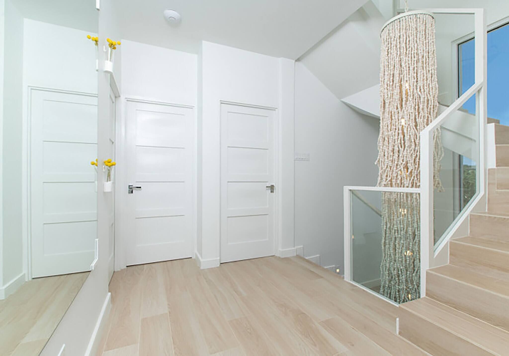 Un interior moderno con una escalera, puertas blancas y barandilla de cristal.