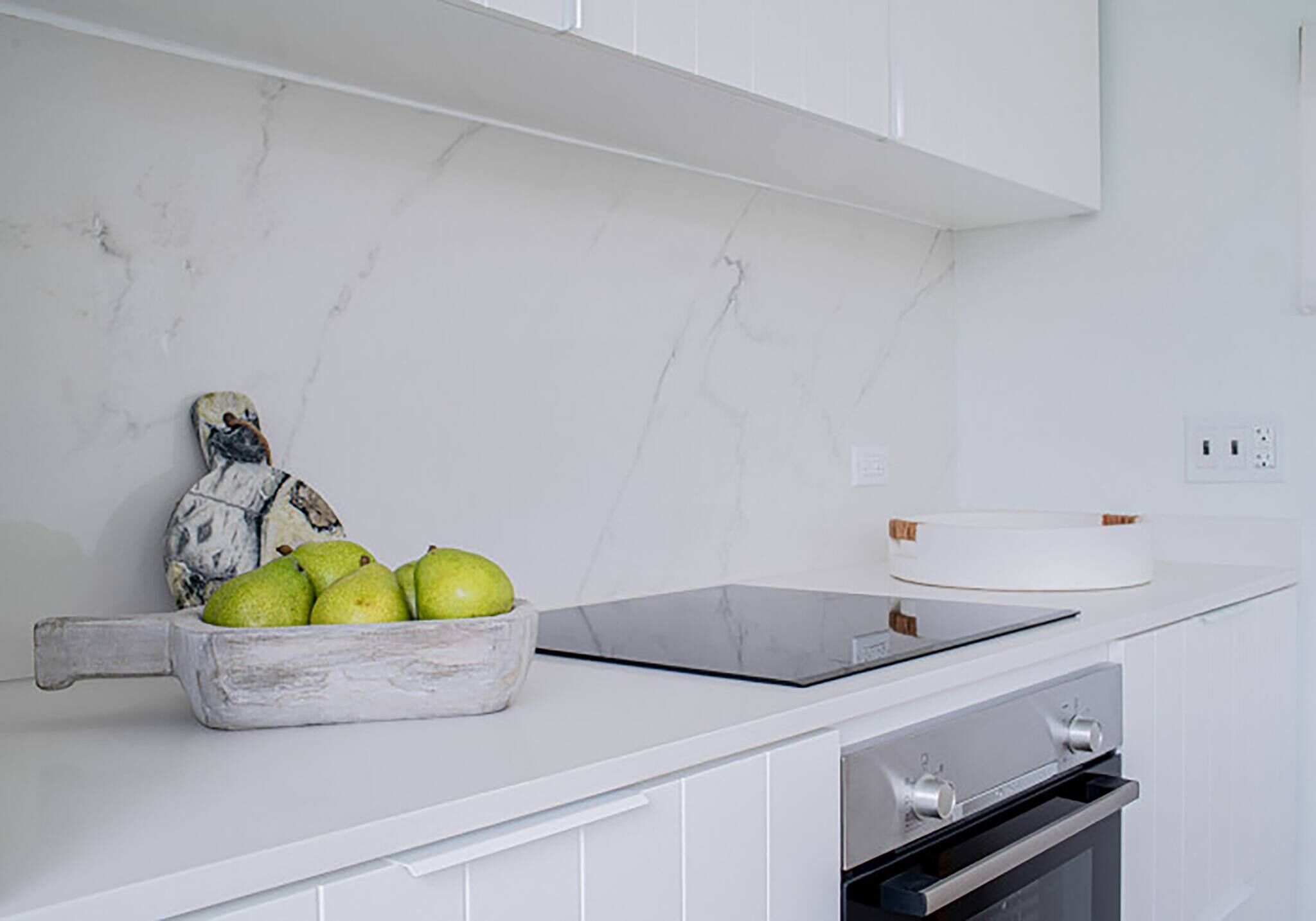 A kitchen with a marble countertop, a bowl of fruit, a cutting board, and an oven.