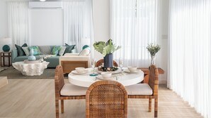 Una sala de estar moderna con comedor, que incluye una mesa redonda, sillas de mimbre y un sofá verde.