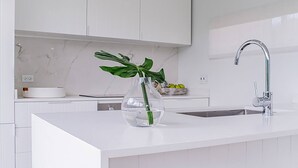 Una cocina moderna con armarios blancos, encimera blanca, un florero de vidrio con una planta verde y un grifo de acero inoxidable.