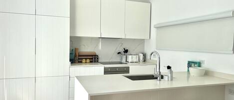 Una cocina moderna con muebles blancos, una isla central con taburetes y un horno empotrado.