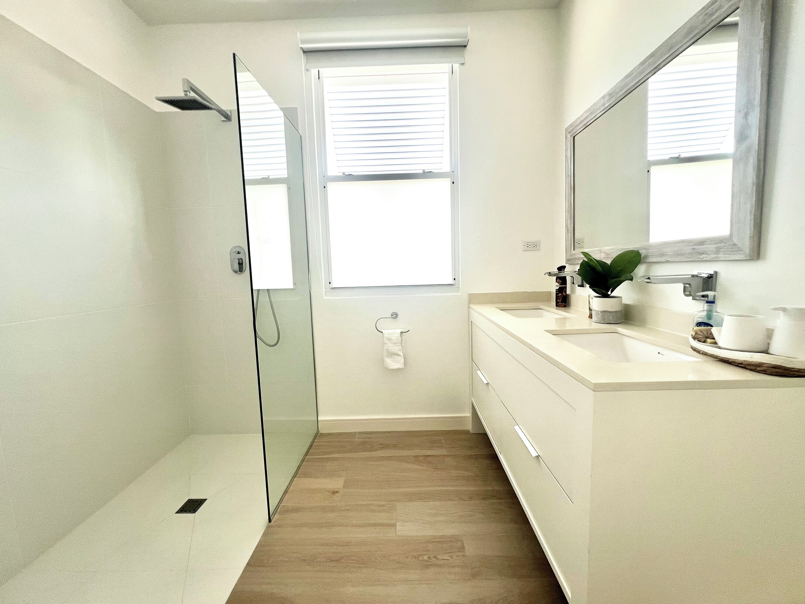 Une salle de bain moderne avec une douche à parois de verre, un meuble-lavabo avec un miroir et une fenêtre équipée de stores.
