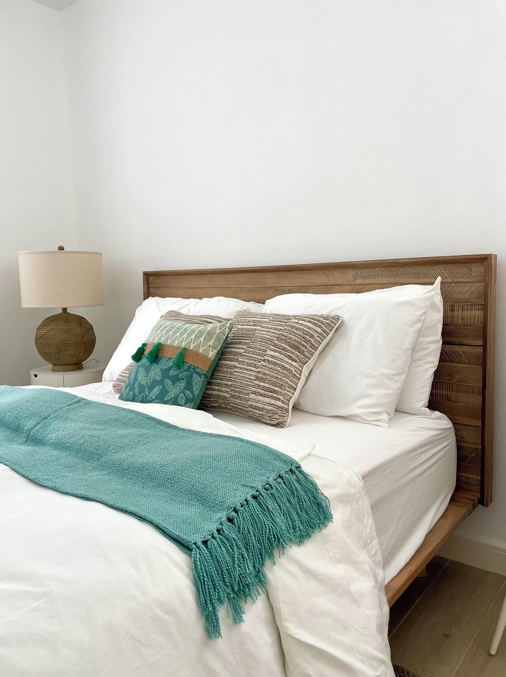 A neatly made bed with white linens, a teal throw blanket, and a variety of patterned pillows.