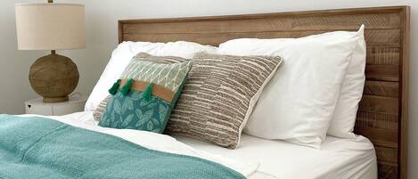 A neatly made bed with white linens, a teal throw blanket, and a variety of patterned pillows.