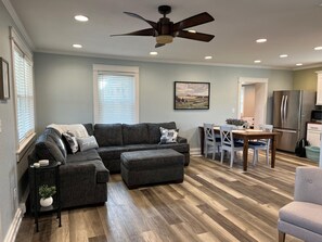 A modern living room with a sectional sofa, a dining table with chairs, a kitchen area with a refrigerator, and a ceiling fan. - Cozy cottage that allows for pets, the experience of outdoors, and the big city! (Monclova)