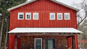 A red wooden building with a stone foundation, a front porch, and a black door. - Modern Rustic Retreat- King bed, hot tub, wineries, waterfalls, hiking, Cornell (Ithaca)