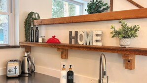 A kitchen with wooden shelves displaying the word "HOME," a stainless steel sink, a toaster, and a kettle. - Modern Rustic Retreat- King bed, hot tub, wineries, waterfalls, hiking, Cornell (Ithaca)