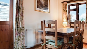 A wooden dining table with chairs, a framed picture on the wall, and a window with curtains. - The Old Stable - Meadowbrook Farm (Moreton, near Thame)