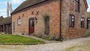 A brick building with a pitched roof, a wooden door, and a small garden area with gravel and grass. - The Old Stable - Meadowbrook Farm (Moreton, near Thame)