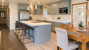 A modern kitchen with a central island, bar stools, a dining table, and a microwave. - Mauka Sunrise, Walk to Hau‘ula Beach & Trails, A/C (Hauula)