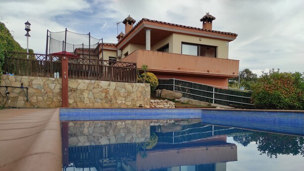 A house with a swimming pool, stone walls, and a metal fence.