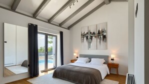 A modern bedroom with a large bed, a view of a swimming pool, and a ceiling with exposed beams.
