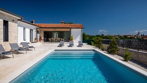 A modern villa with a swimming pool, outdoor seating, and a view of the surrounding landscape.
