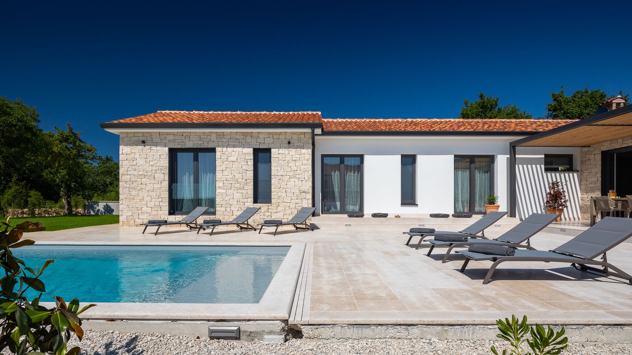 A modern house with a swimming pool, stone walls, and a tiled roof.