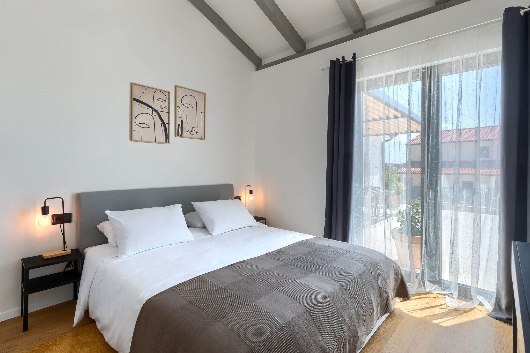 Un dormitorio con cama, mesitas de noche, decoración en la pared y un ventanal con cortinas.