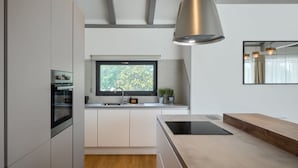 A modern kitchen with white cabinetry, a built-in oven, a window with a view of greenery, and a pendant light.