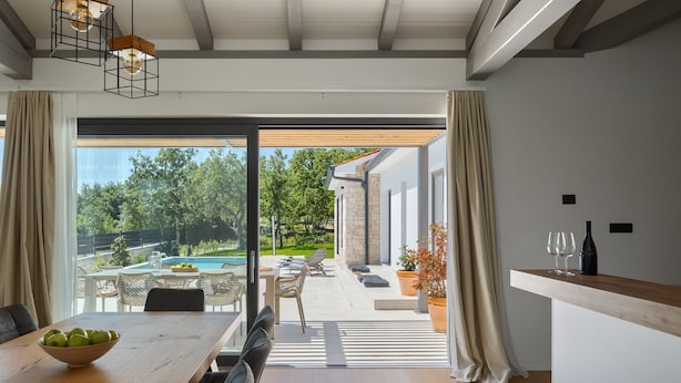A modern kitchen with a large window, a dining area with a wooden table, and a view of a pool and garden.