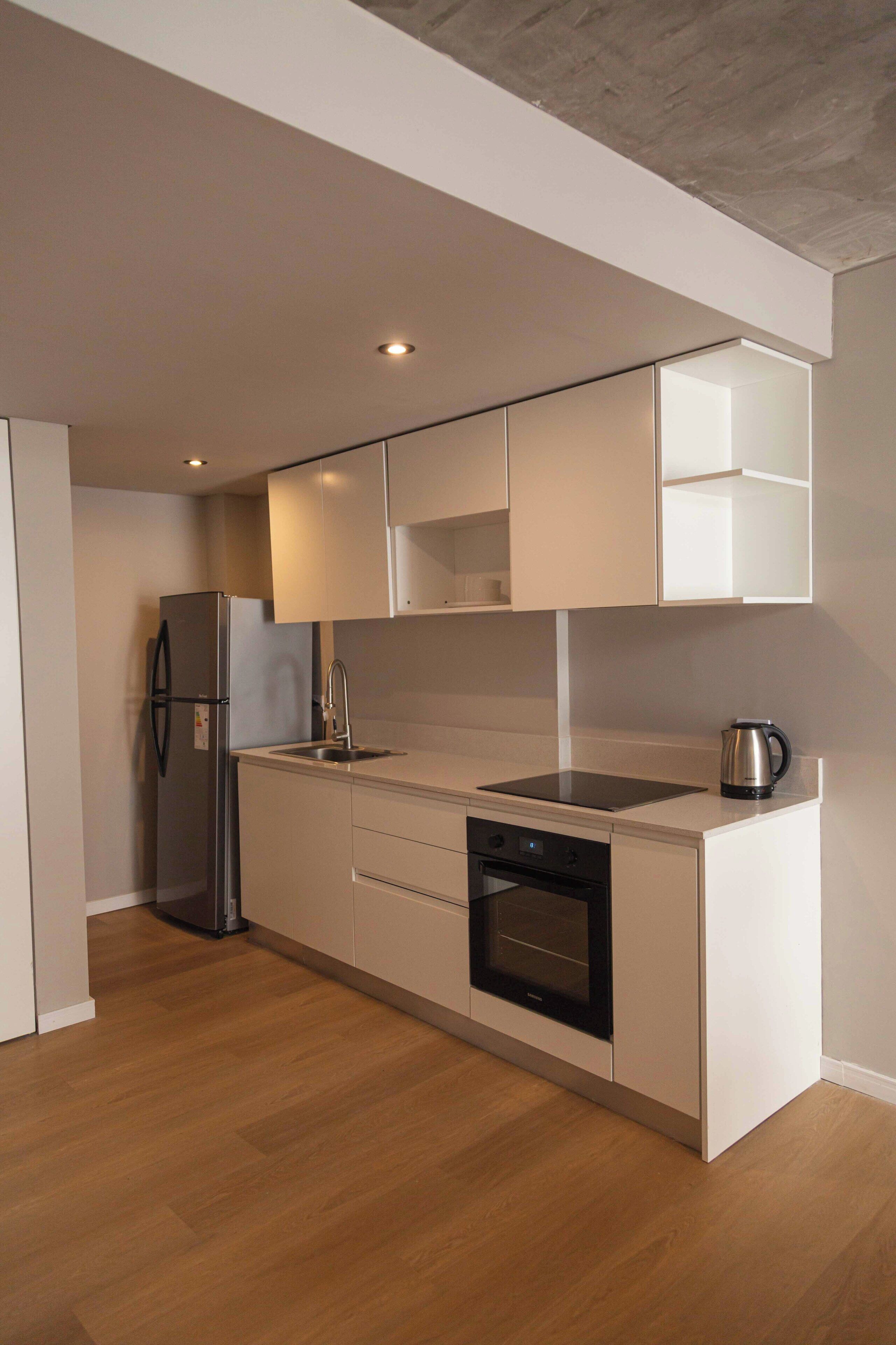 Una cocina moderna con muebles blancos, un refrigerador de acero inoxidable, un horno empotrado y una tetera sobre la encimera.