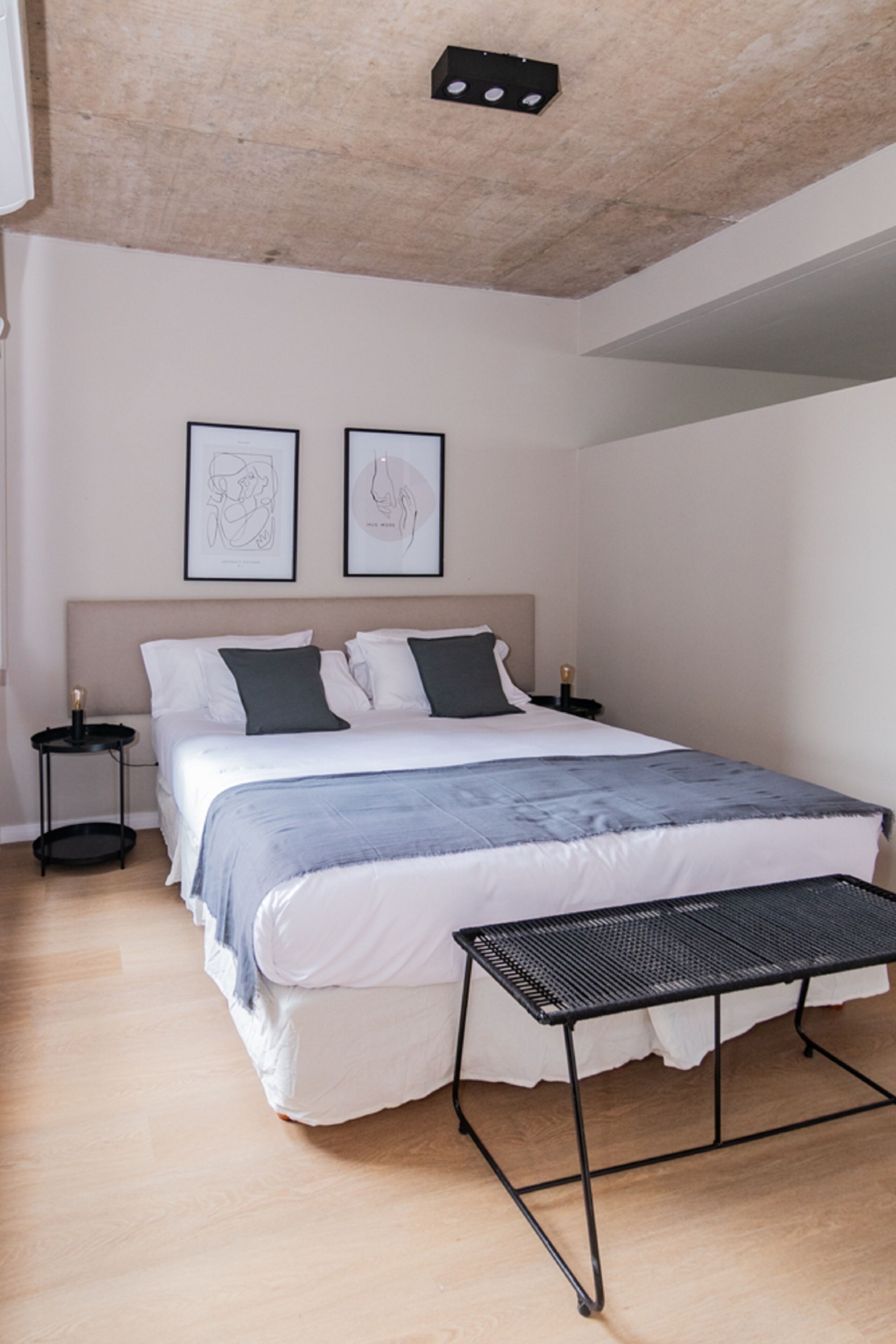 A bedroom with a bed, two bedside tables, a small table, and two framed artworks on the wall.