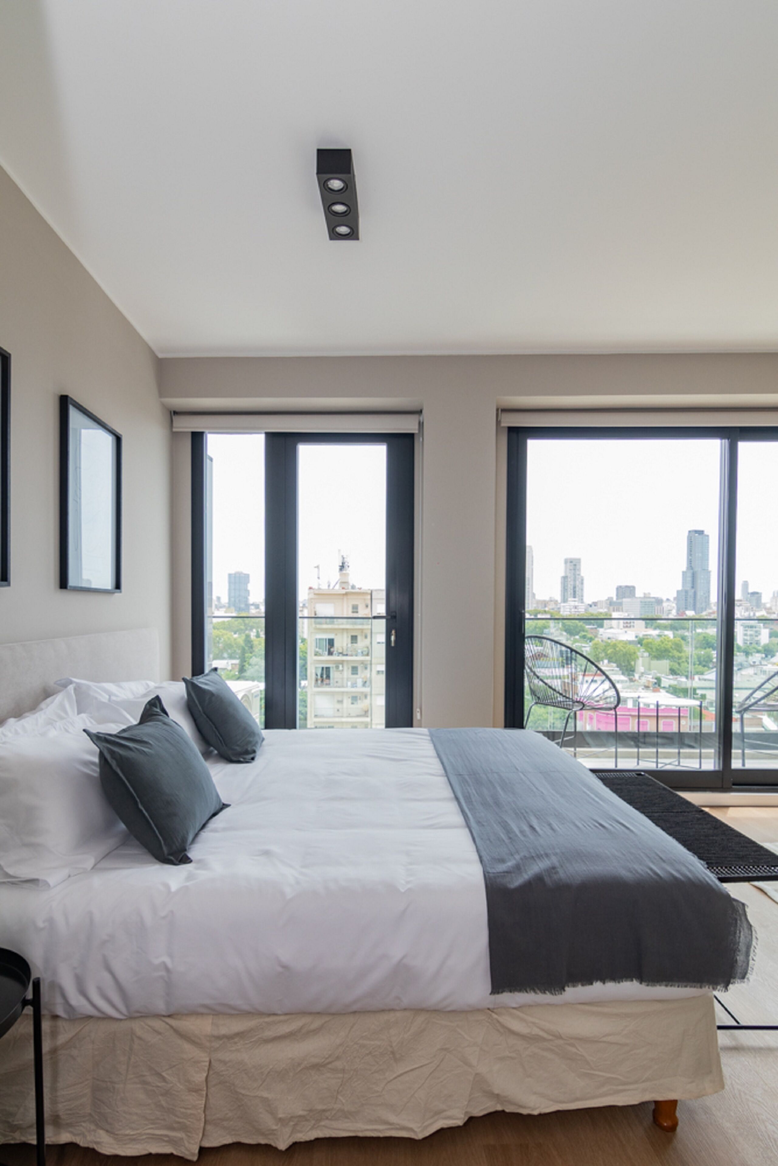 A modern bedroom with a large bed, city views through the windows, and a cityscape visible outside.