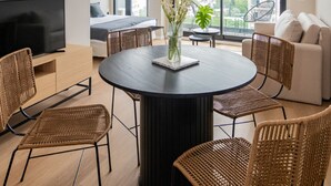 A modern living room with a round black table, wicker chairs, a flat-screen TV, and a large window offering a city view. - Milenia Soho by iPPA (Buenos Aires)
