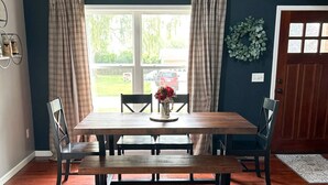 Une salle à manger avec une table en bois, quatre chaises, un banc et une fenêtre avec des rideaux.