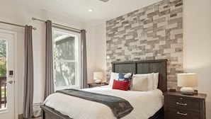 Een slaapkamer met een bed, nachtkastjes, een wand met steenmotief en een deur voorzien van gordijnen.
