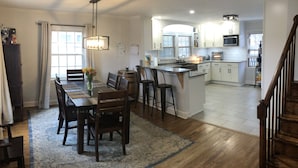 A spacious kitchen with a central island, wooden flooring, and a dining area with a table and chairs. - Spacious 6BR, 10 bed Derby House. Walk to the track. (Louisville)