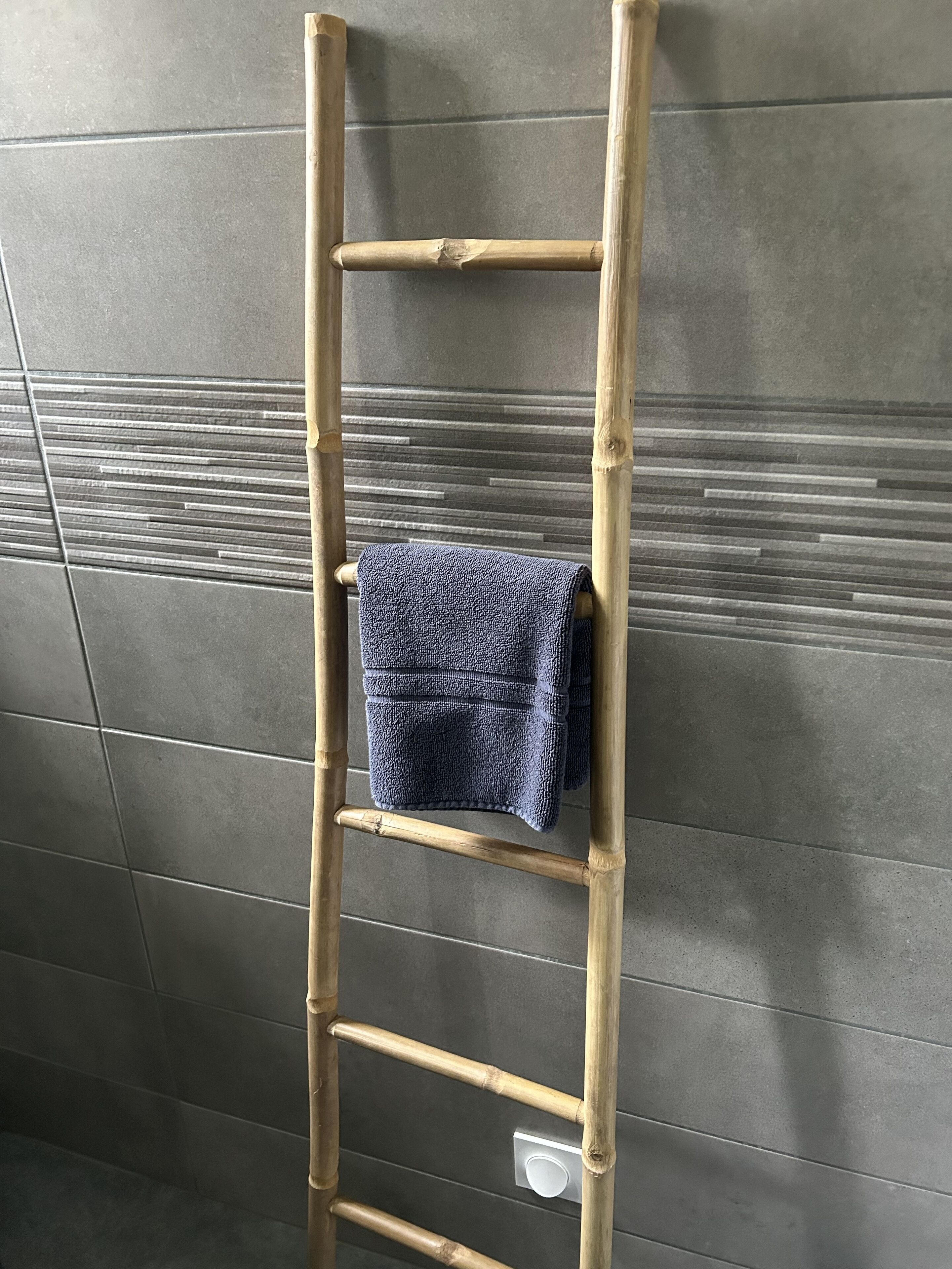 Une échelle en bambou, avec une serviette pliée qui y est suspendue, appuyée contre un mur recouvert de carreaux.
