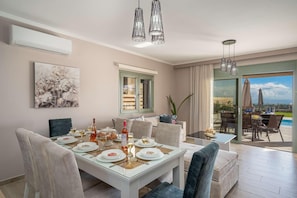 A dining area with a table set for four, a painting on the wall, and a view of the outdoors. - Ionian residence  (Kefalonia)