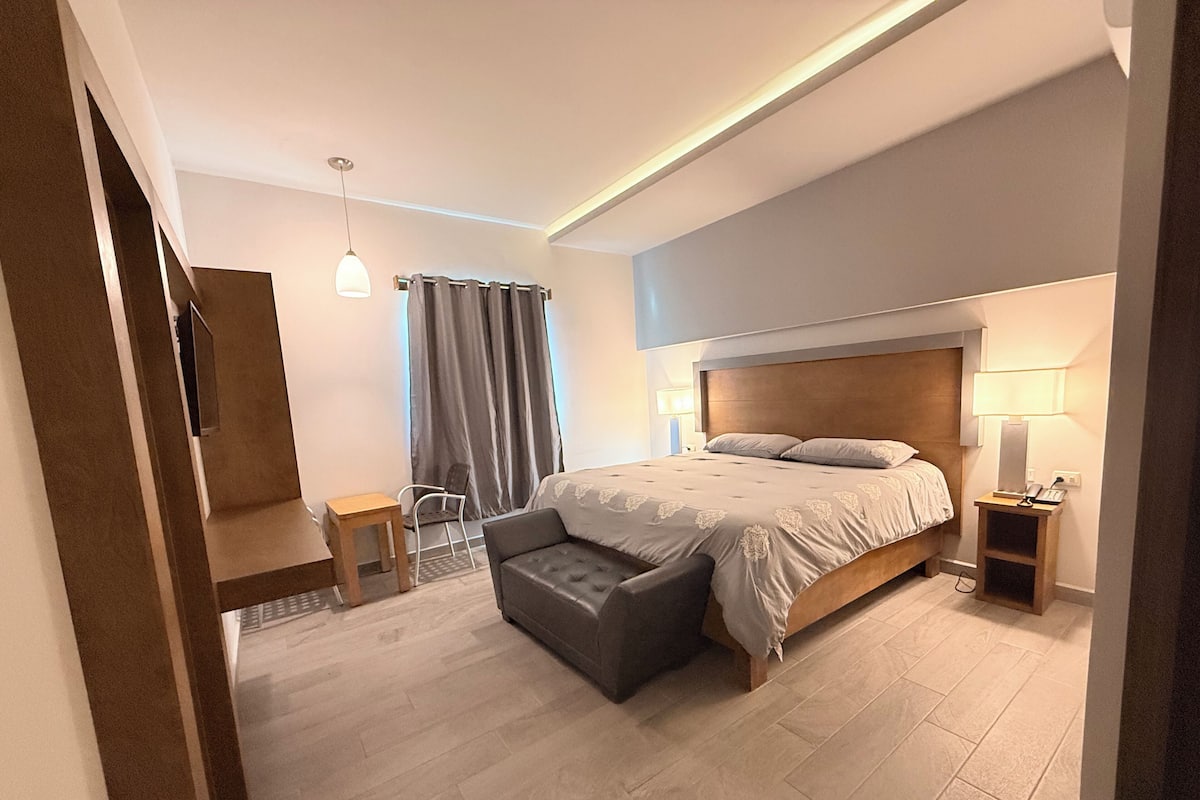 Un dormitorio moderno con una cama grande, mesitas de noche, un escritorio y una silla.